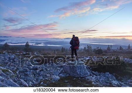 Picture - Hiker enjoying sunset on cliff top, Sarkitunturi, Lapland, Finland. Fotosearch