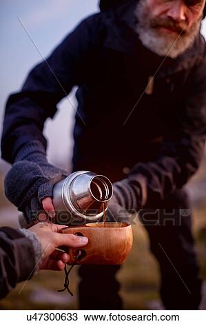 Stock Image - Hiker pouring coffee into friend's cup. Fotosearch