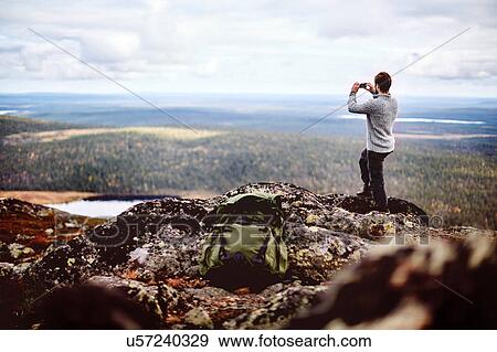 Stock Photo - Hiker taking photograph on cliff top, Keimiotunturi, Lapland, Finland. Fotosearch