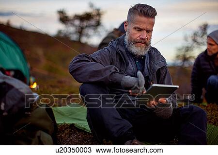 Stock Image - Hiker using digital tablet by tent, Keimiotunturi, Lapland, Finland. Fotosearch