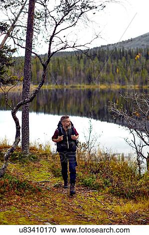 Stock Image - Hiker walking by lake, Kesankijarvi, Lapland, Finland. Fotosearch