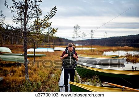 Stock Image - Hiker walking by lake with boats, Kesankijarvi, Lapland, Finland. Fotosearch