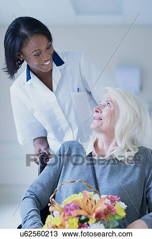 Stock Image - Hospital orderly pushing senior female patient in wheelchair. Fotosearch