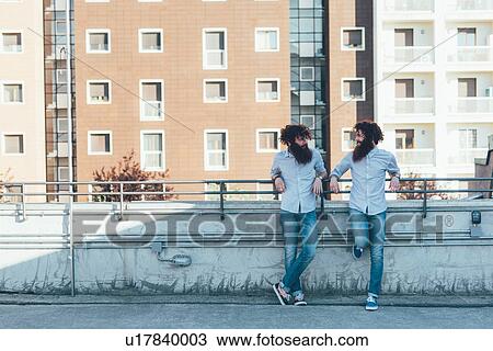 Identical male hipster twins chatting on apartment roof terrace View Large Photo Image Stock Image - Identical male hipster twins chatting on apartment roof terrace. Fotosearch