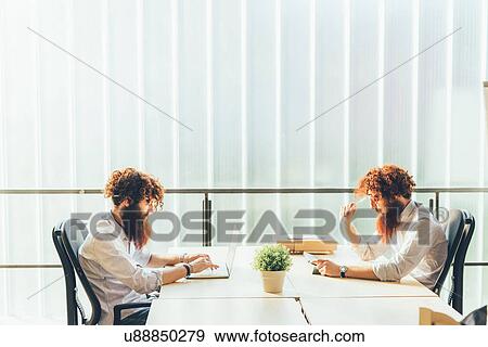 Stock Photo - Identical male hipster twins working on laptop and digital tablet at office desk. Fotosearch