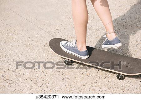 Stock Image - Legs of young female skateboarder skateboarding. Fotosearch