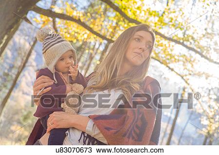 Stock Image - Low angle view of mother in forest holding baby girl. Fotosearch