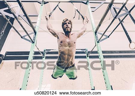 Low angle view of young male cross trainer training on exercise rings in gym View Large Photo Image Picture - Low angle view of young male cross trainer training on exercise rings in gym. Fotosearch