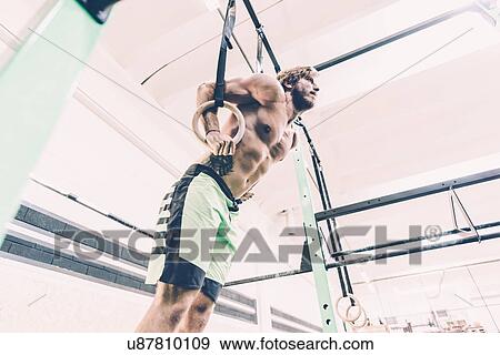 Low angle view of young male cross trainer training on exercise rings in gym View Large Photo Image Stock Photo - Low angle view of young male cross trainer training on exercise rings in gym. Fotosearch