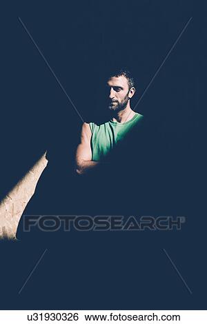 Stock Photograph - Low key portrait of young man with folded arms staring from shadows. Fotosearch