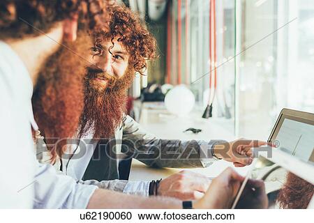 Stock Image - Male adult hipster twins pointing at laptop in office. Fotosearch