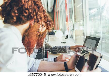 Stock Photography - Male adult hipster twins pointing at laptop in office. Fotosearch