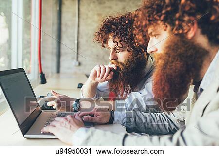 Stock Image - Male adult hipster twins working on laptop in office. Fotosearch