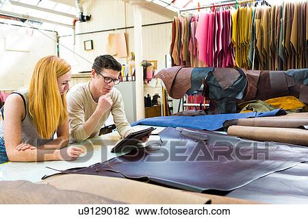 Stock Image - Male and female colleagues working together, looking at digital tablet in leather jacket manufacturers. Fotosearch