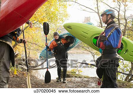 Stock Photography - Male and female kayakers carrying kayaks on banks of River Dee. Fotosearch