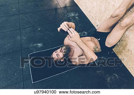 Male cross trainer reading smartphone whilst lying on back in gym View Large Photo Image Stock Image - Male cross trainer reading smartphone whilst lying on back in gym. Fotosearch