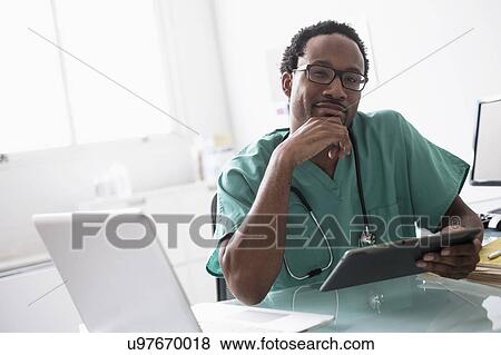 Stock Photo - Male doctor working with digital tablet at desk. Fotosearch