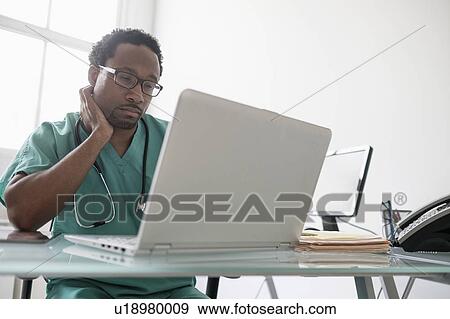 Stock Photo - Male doctor working with laptop at desk. Fotosearch
