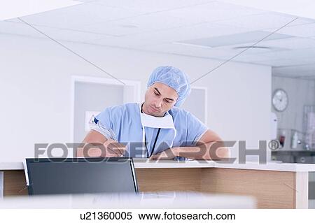 Stock Photography - Male doctor writing medical notes at nurses station in hospital. Fotosearch
