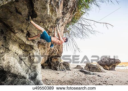 Stock Photo - Male free climber climbing rock overhang on Pandawa Beach, Bali, Indonesia. Fotosearch