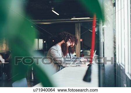 Picture - Male hipster twins working on laptop at office desk. Fotosearch