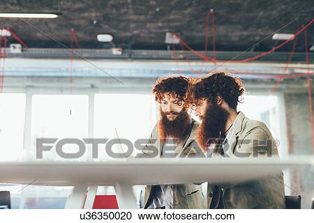 Male hipster twins working on laptop at office desk View Large Photo Image Stock Image - Male hipster twins working on laptop at office desk. Fotosearch
