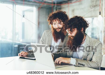 Male hipster twins working on laptop at office desk View Large Photo Image Stock Image - Male hipster twins working on laptop at office desk. Fotosearch