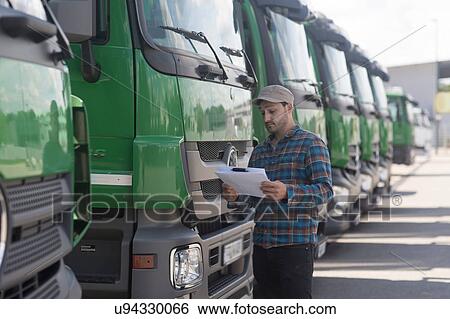 Stock Photograph - Man by fleet of trucks looking at paperwork. Fotosearch