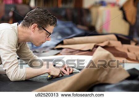 Stock Image - Man cutting leather with utility knife in leather jacket manufacturers. Fotosearch