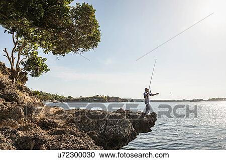 Stock Image - Man fishing from rocks, Pink Beach, Lombok, Indonesia. Fotosearch