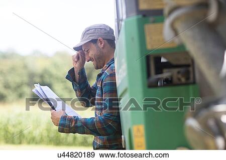 Stock Photo - Man leaning against truck looking at paperwork smiling. Fotosearch