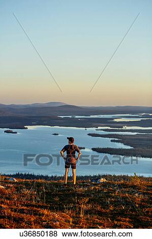 Stock Photo - Man looking out to lake on cliff top at sunset, Keimiotunturi, Lapland, Finland. Fotosearch