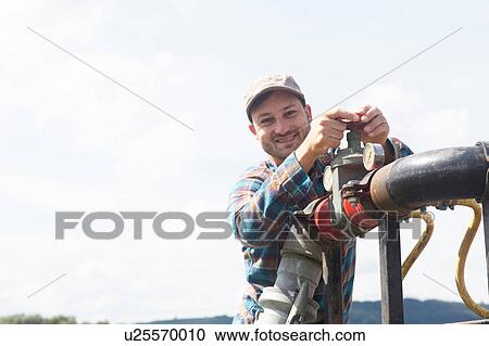 Man opening valve on industrial piping, looking at camera smiling View Large Photo Image Stock Image - Man opening valve on industrial piping, looking at camera smiling. Fotosearch