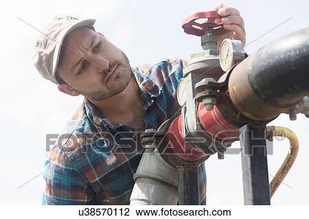 Stock Image - Man opening valve on industrial piping. Fotosearch