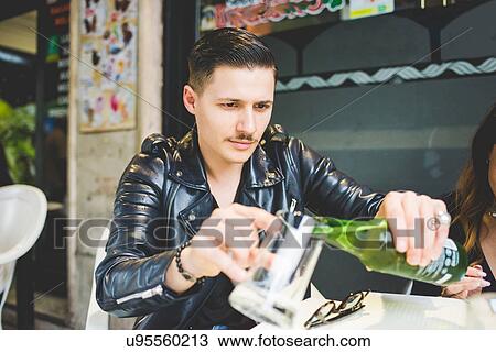 Stock Image - Man pouring beer into mug at sidewalk cafe. Fotosearch