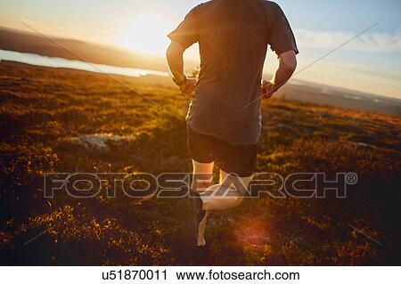 Stock Image - Man running on cliff top at sunset, Keimiotunturi, Lapland, Finland. Fotosearch