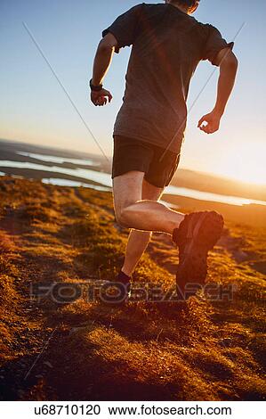 Stock Image - Man running on cliff top at sunset, Keimiotunturi, Lapland, Finland. Fotosearch