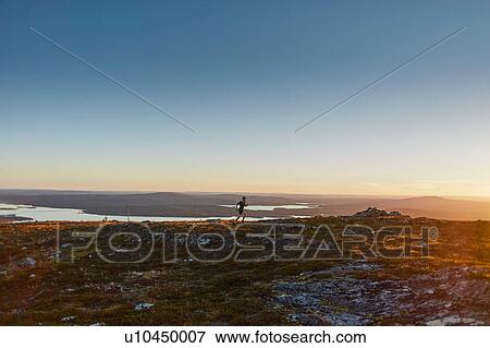 Stock Photo - Man running on cliff top at sunset, Keimiotunturi, Lapland, Finland. Fotosearch