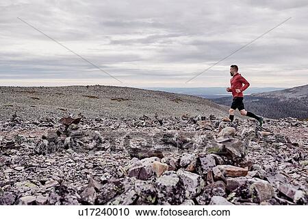 Stock Image - Man running on rocky cliff top, Kesankitunturi, Lapland, Finland. Fotosearch