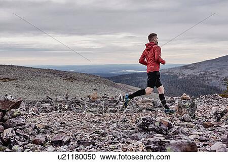Stock Image - Man running on rocky cliff top, Kesankitunturi, Lapland, Finland. Fotosearch