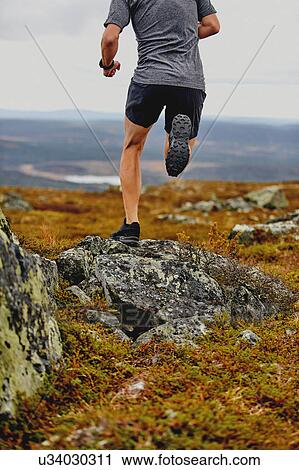 Stock Image - Man running on rocky cliff top, Keimiotunturi, Lapland, Finland. Fotosearch