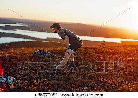 Stock Image - Man stretching on cliff top at sunset, Keimiotunturi, Lapland, Finland. Fotosearch