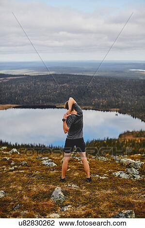 Stock Image - Man stretching on rocky cliff top, Keimiotunturi, Lapland, Finland. Fotosearch