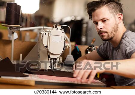 Picture - Man using sewing machine to sew leather in leather jacket manufacturers. Fotosearch