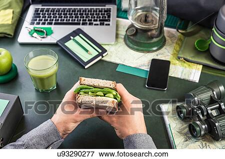 Mans hand's holding sandwich at table with hiking equipment and laptop View Large Photo Image Stock Photo - Mans hand's holding sandwich at table with hiking equipment and laptop. Fotosearch