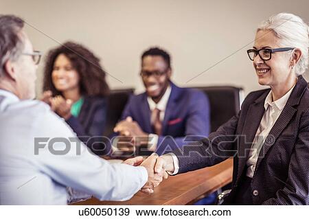 Stock Photo - Mature businesswoman shaking hands with client at boardroom meeting. Fotosearch