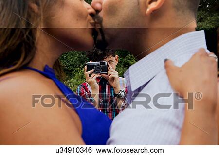 Mature couple outdoors, kissing, son taking photograph of them, using camera View Large Photo Image Stock Photograph - Mature couple outdoors, kissing, son taking photograph of them, using camera. Fotosearch