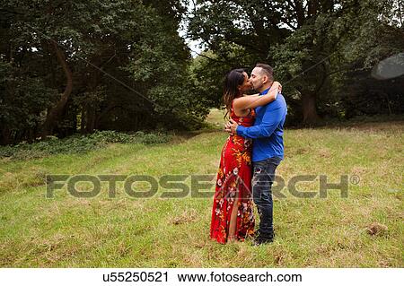 Stock Image - Mature couple outdoors, standing in field, kissing. Fotosearch