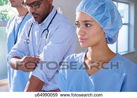 Stock Photo - Mature male doctor with two medics rolling up sleeves on hospital ward. Fotosearch