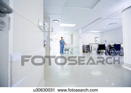 Stock Image - Medics pushing hospital bed along corridor. Fotosearch